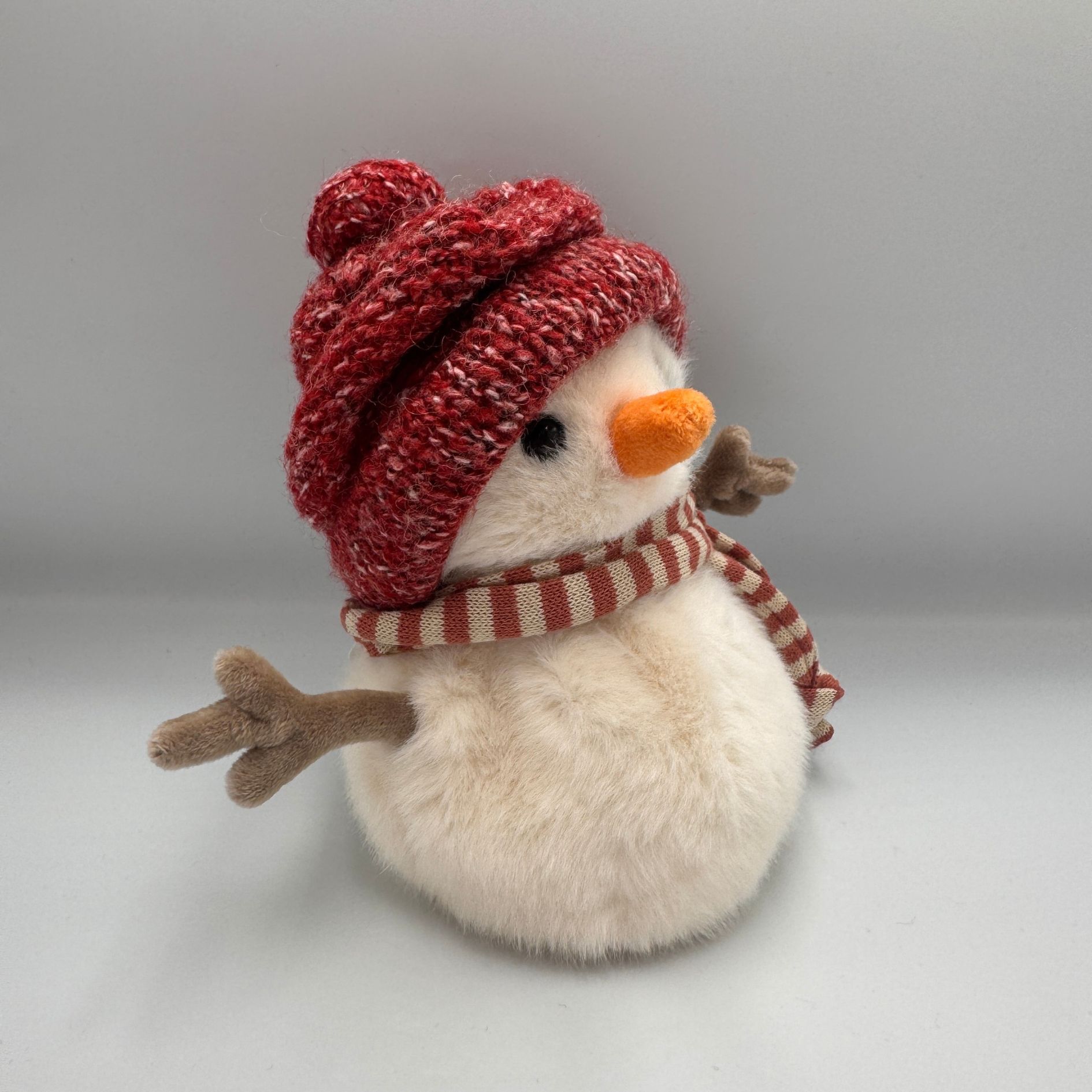 Bałwan Bukowski Jimmy the Little Snowman 15 cm w czerwonej czapce z pomponem i czerwono-beżowym szaliku.